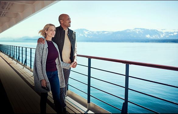 Happy couple taking in a view of Alaskan mountains from the deck of a cruise ship