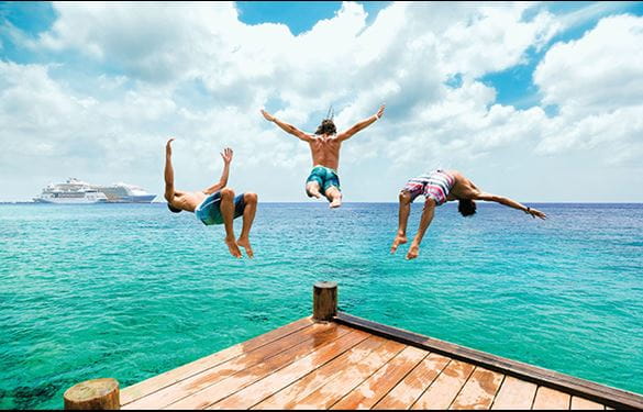 Three boys diving off of a wooden platform into the ocean